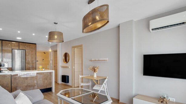 Un salon moderne comprenant un canapé, une table basse en verre, un téléviseur et un coin cuisine avec un réfrigérateur et un four à micro-ondes.