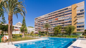 Une piscine à l’eau d’un bleu limpide, entourée d’une clôture, et un immeuble à plusieurs étages en arrière-plan.