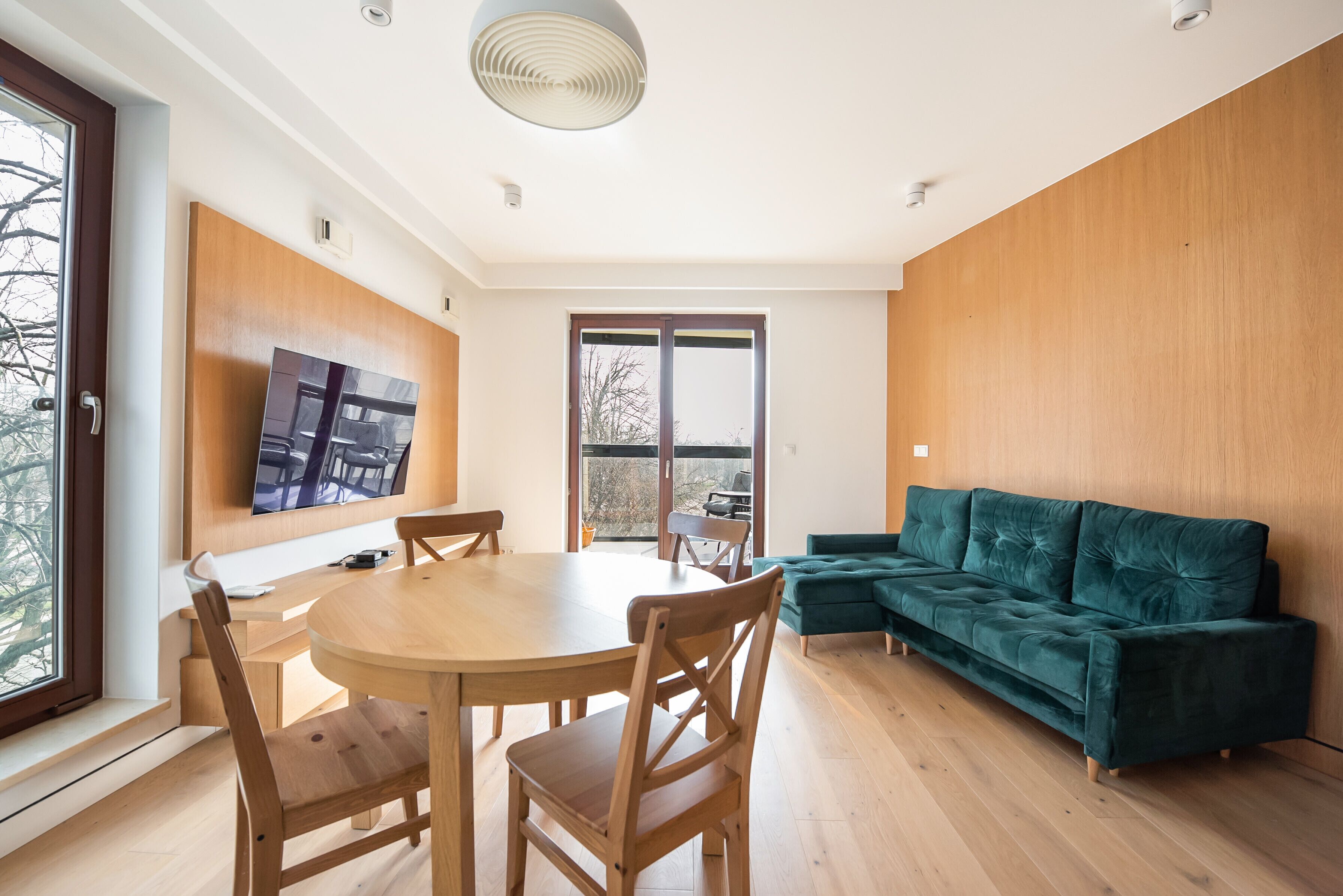 Una sala de estar moderna con una mesa de comedor de madera, sillas, un sofá verde y un televisor grande en la pared.