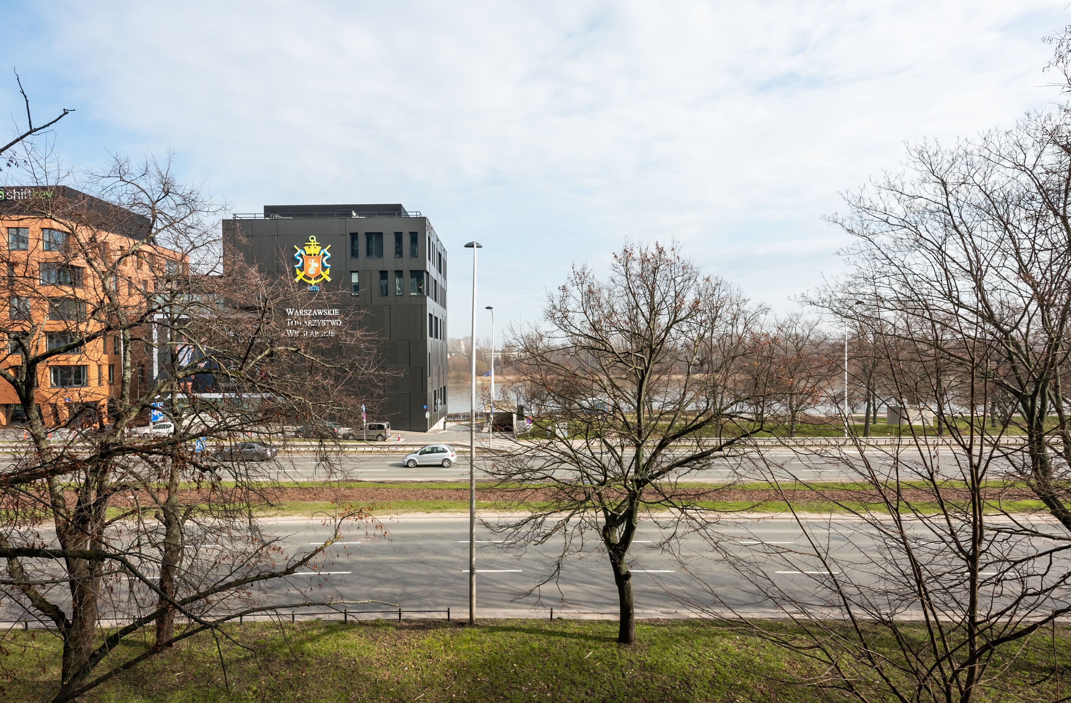 A building with a prominent coat of arms and the text "WARSZAWSKIE TOJNYKOWY WNUKI W NAKOJE."