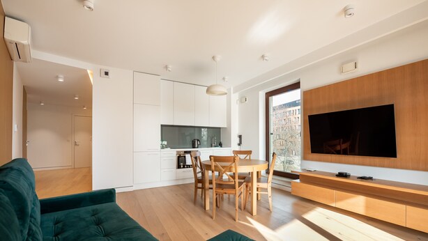 Ein modernes Wohnzimmer mit einem grünen Sofa, einem Holzesstisch und einem an einer Holzwand montierten Fernseher.
