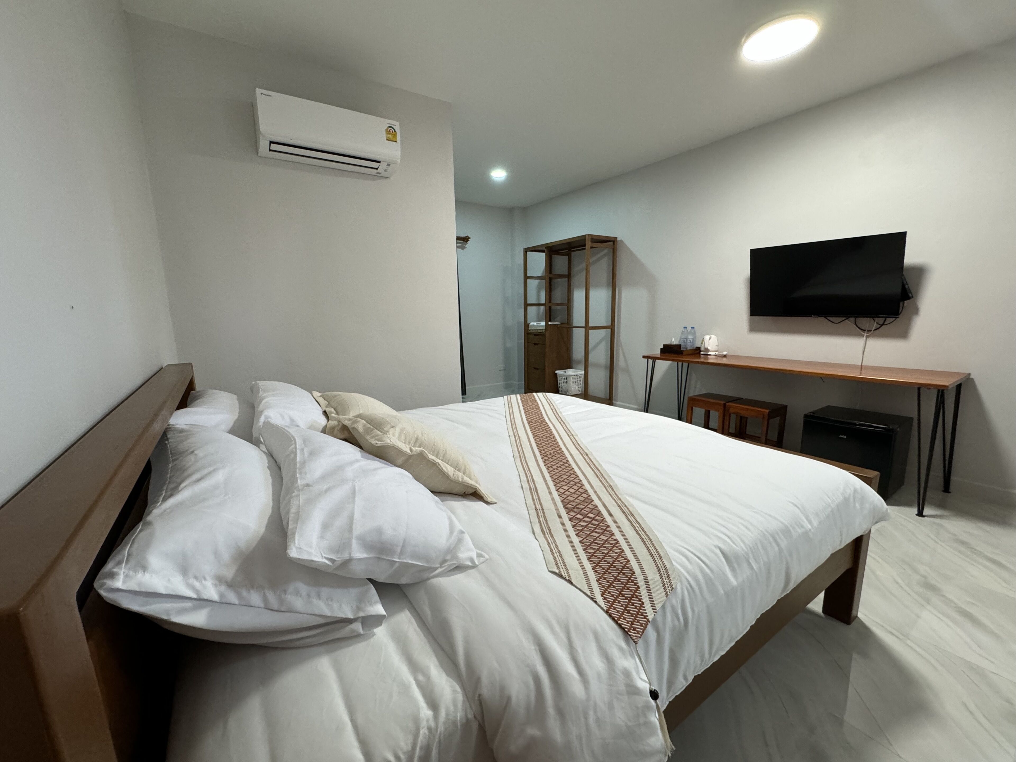 A bedroom with a bed, a desk, a television, and an air conditioning unit.