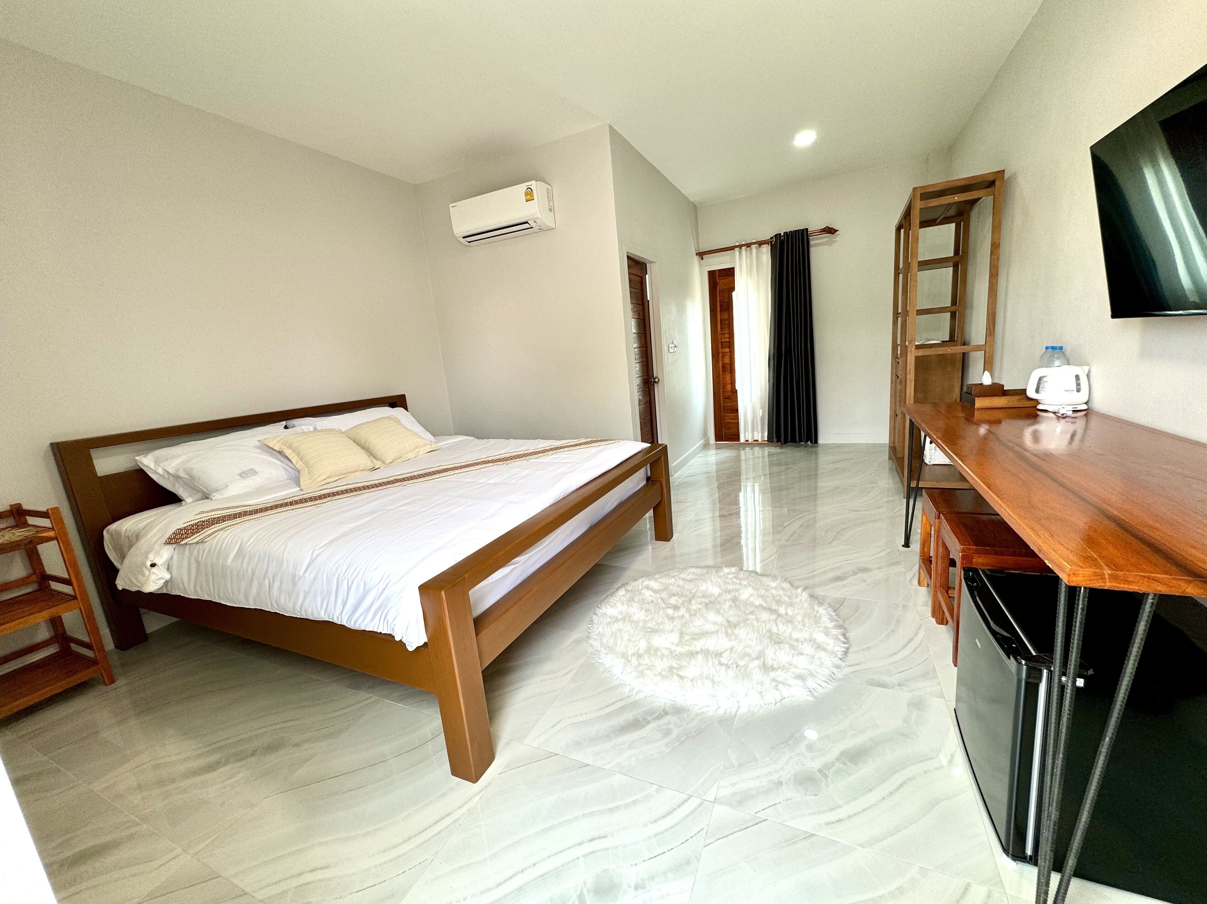 Una habitación de hotel con una cama, un escritorio de madera, un televisor y un equipo de aire acondicionado.