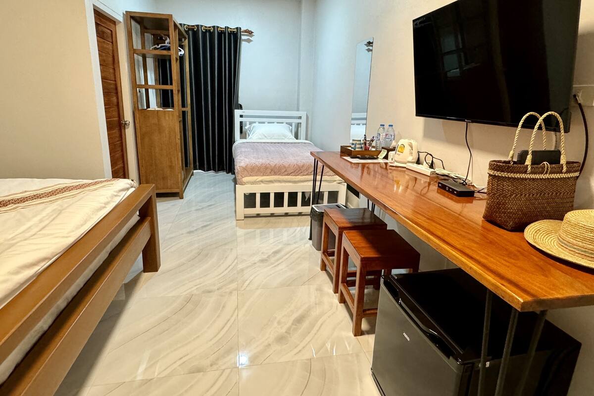 A hotel room with a bed, a desk with a chair, a television, a refrigerator, and a wooden wardrobe.