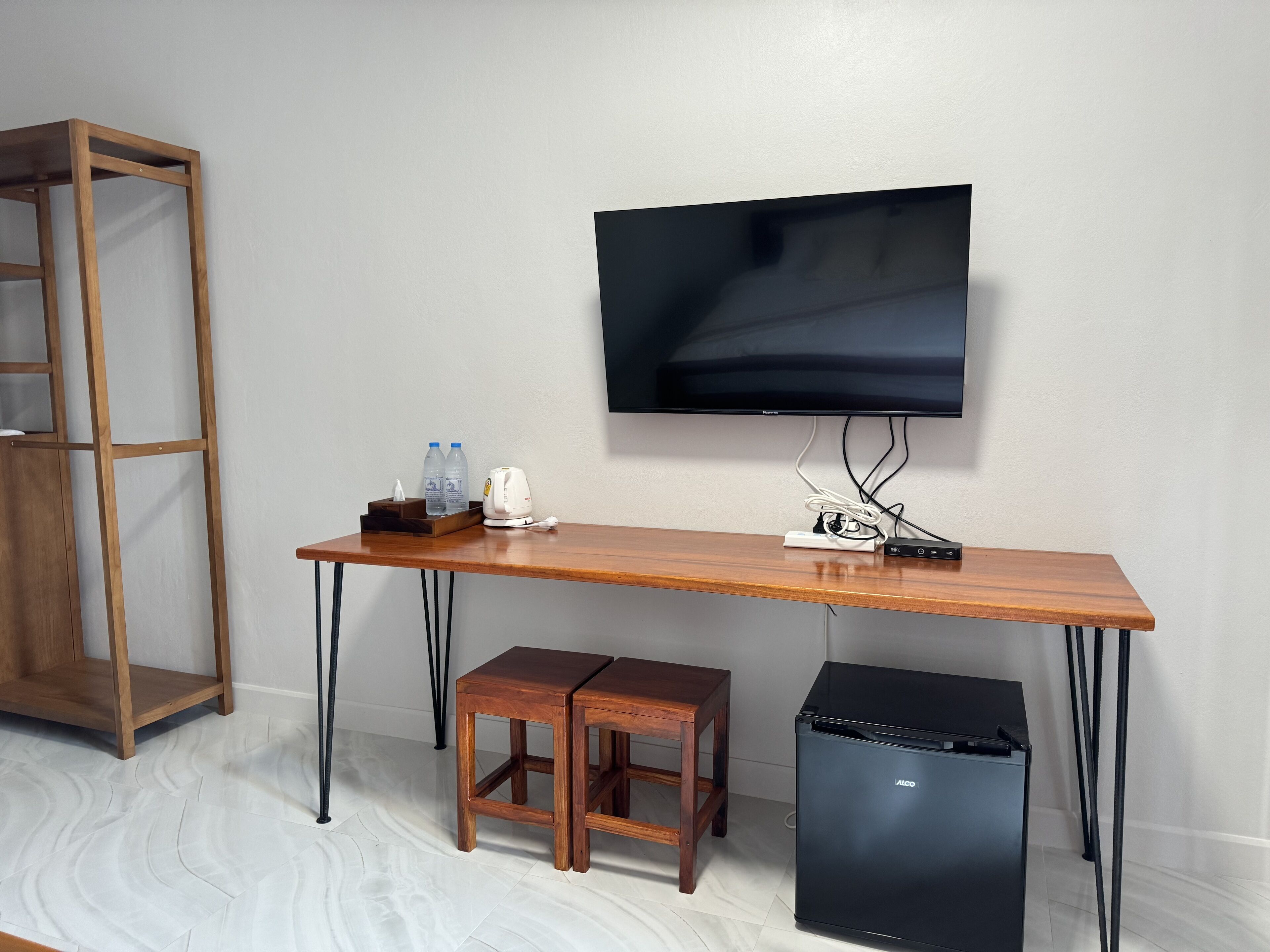 Una habitación con un escritorio de madera, un refrigerador negro, un televisor en la pared y un armario de madera.