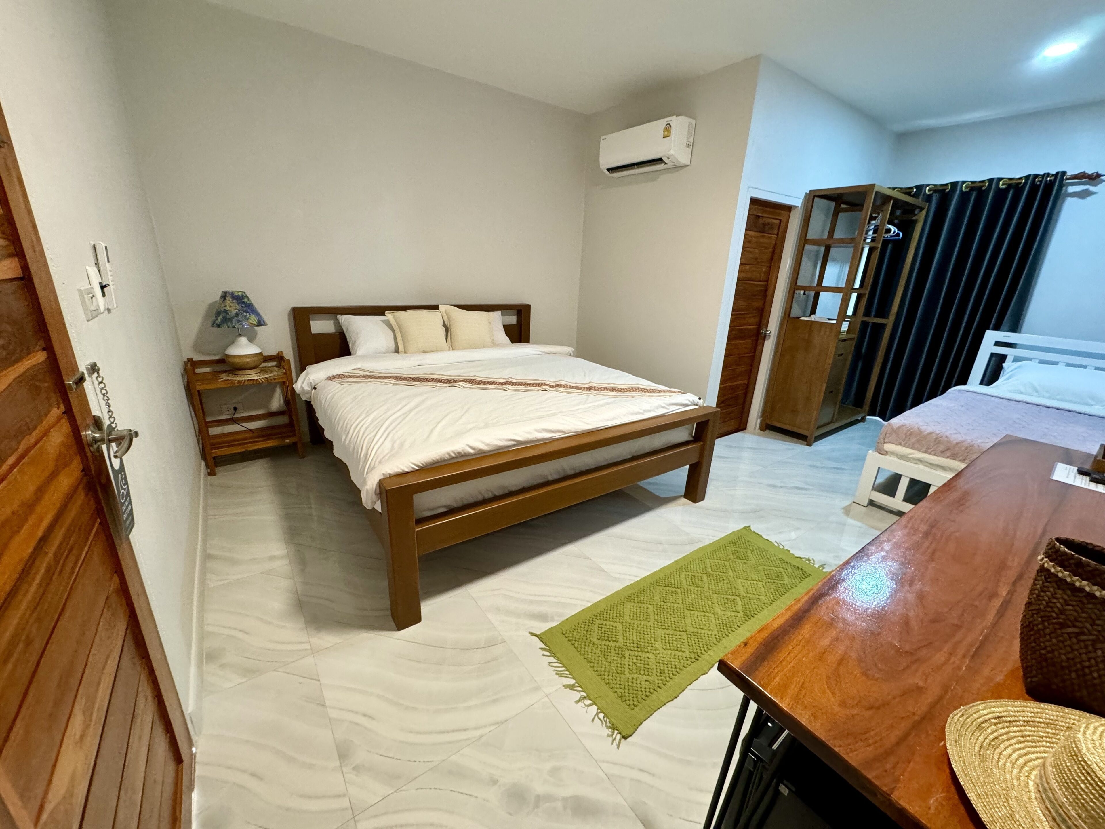 A bedroom with a wooden bed, a nightstand with a lamp, a green rug, and a wooden desk with a chair.