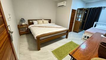 A bedroom with a wooden bed, a nightstand with a lamp, a green rug, and a wooden desk with a chair.
