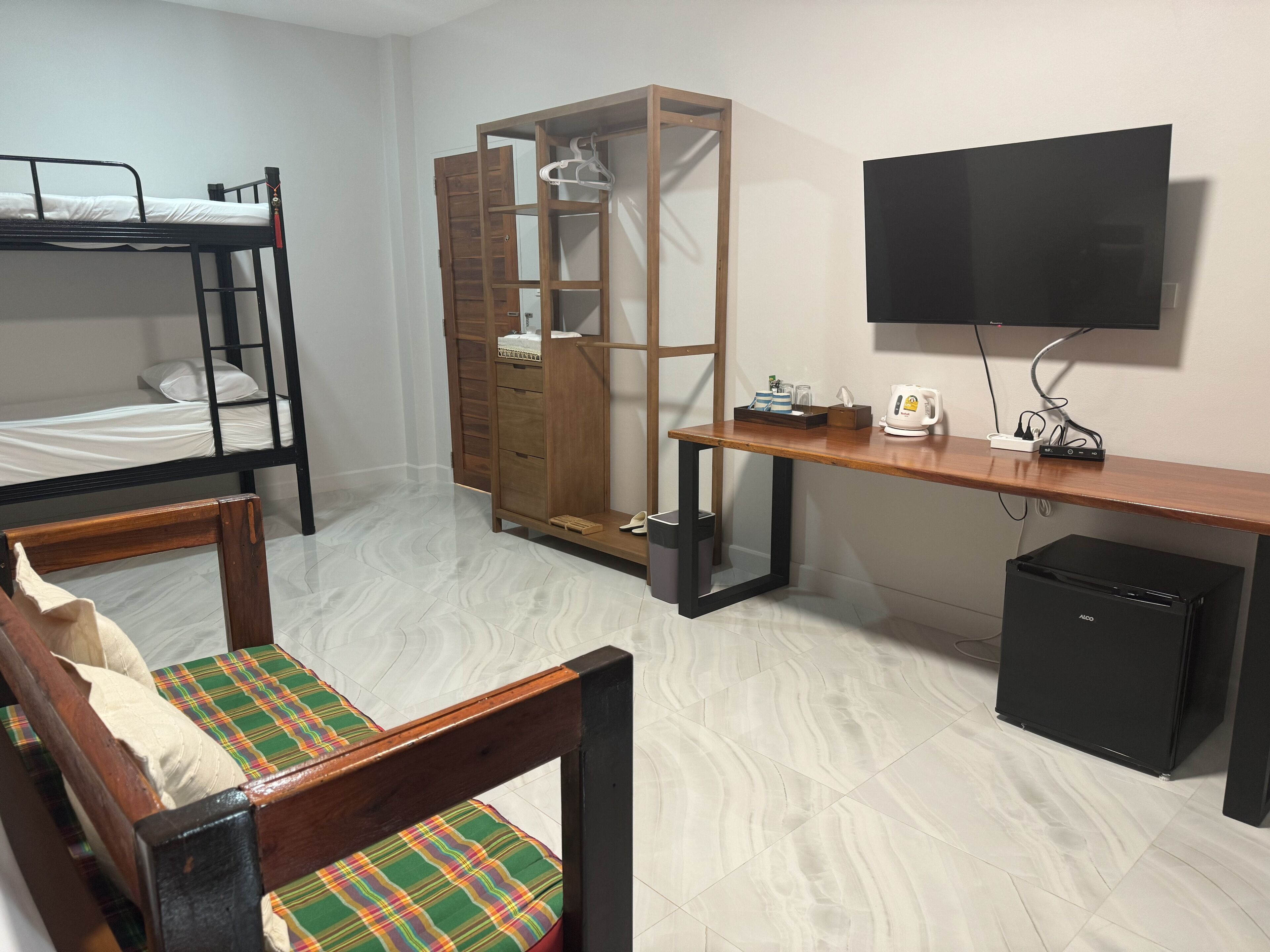 Une chambre de type dortoir, avec des lits superposés, un bureau avec un ordinateur, une télévision et un petit réfrigérateur.
