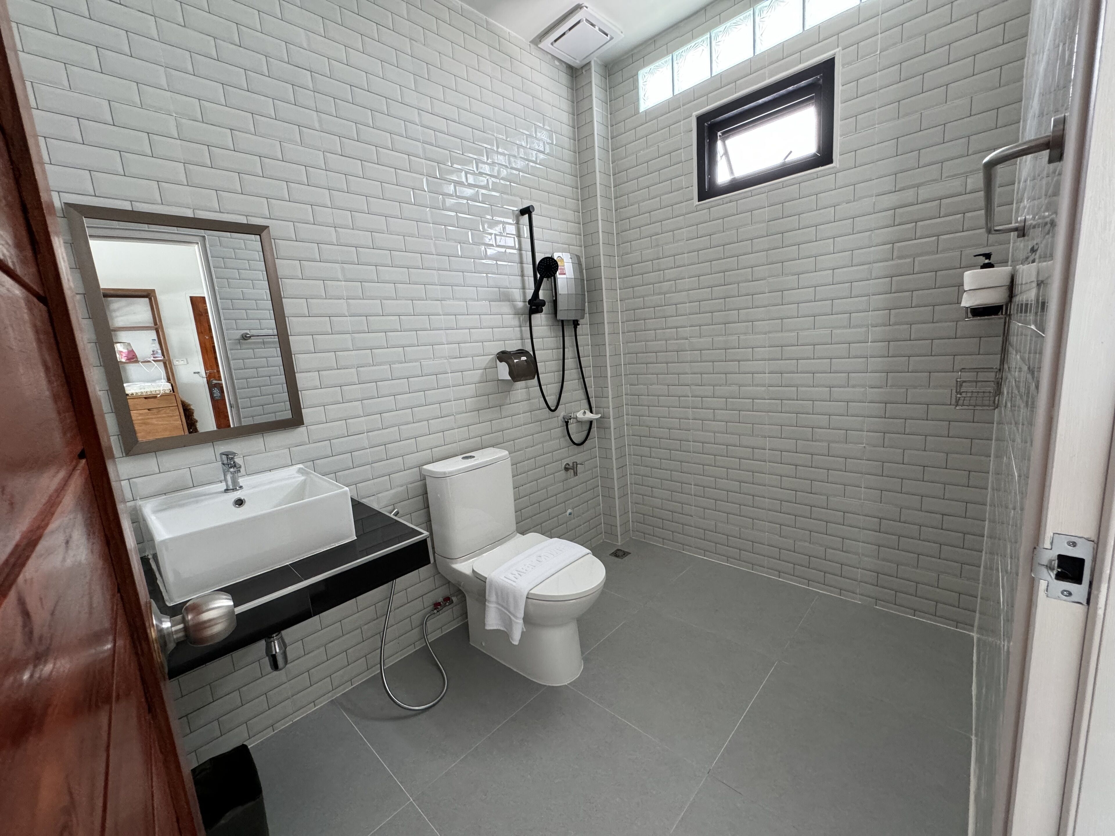 A modern bathroom with white brick walls, a large mirror, a sink, toilet, and a shower.