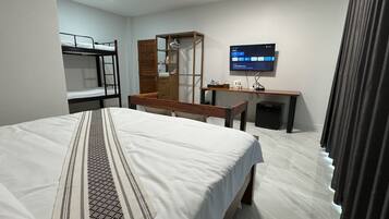 Quarto de hotel com uma cama de solteiro, uma escrivaninha, uma televisão e um guarda-roupa.