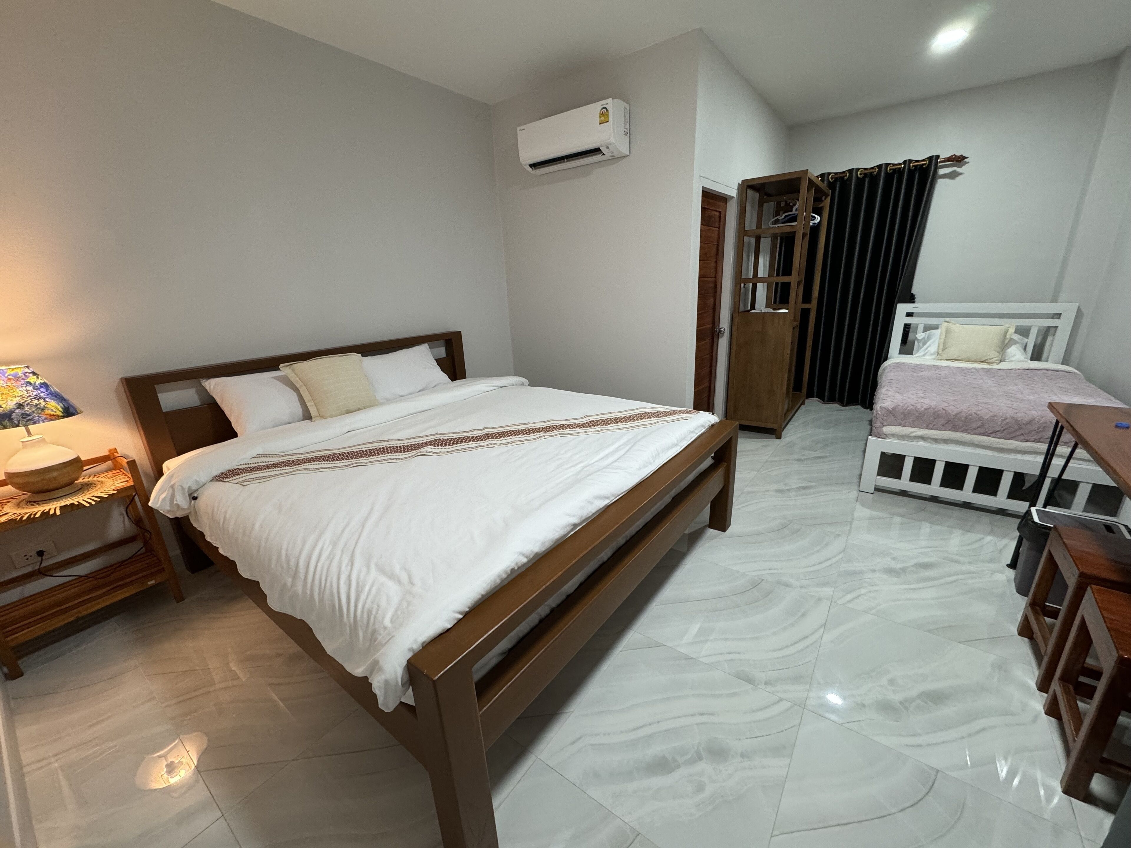 Un dormitorio con cama de madera, una mesita de noche con lámpara, aire acondicionado y un mueble de madera pequeño.