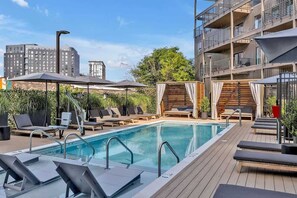 A rooftop pool area with lounge chairs and umbrellas, surrounded by buildings.
