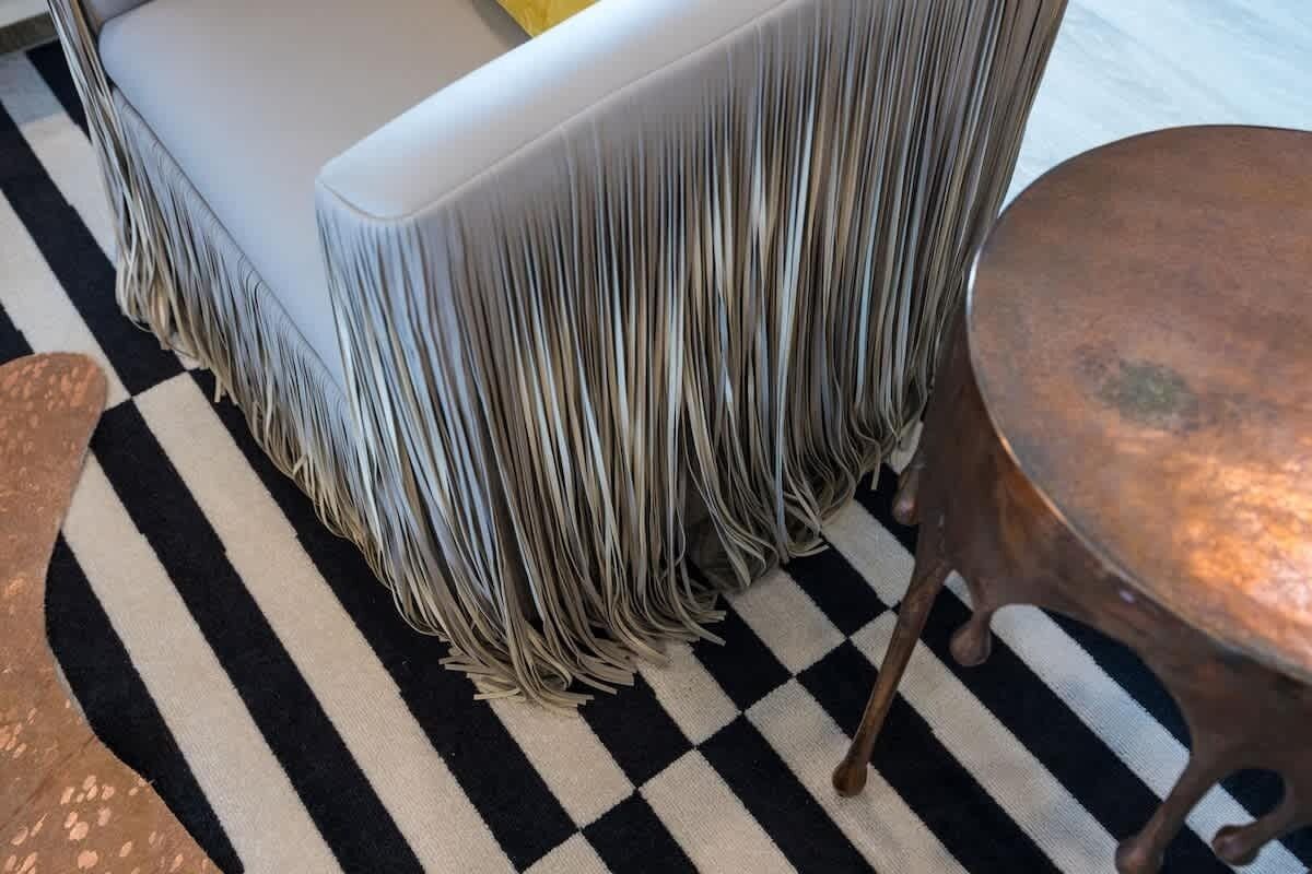 A checkered floor, a white sofa with fringed upholstery, and a round table with a copper top.