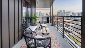 Ein Balkon mit Korbstühlen, einem Tisch und einem gemusterten Teppich, mit Blick auf die Stadt.