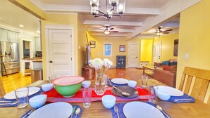 Een eetgedeelte met een tafel voor vier personen, een keuken op de achtergrond en een woonkamer met een bank en een televisie.