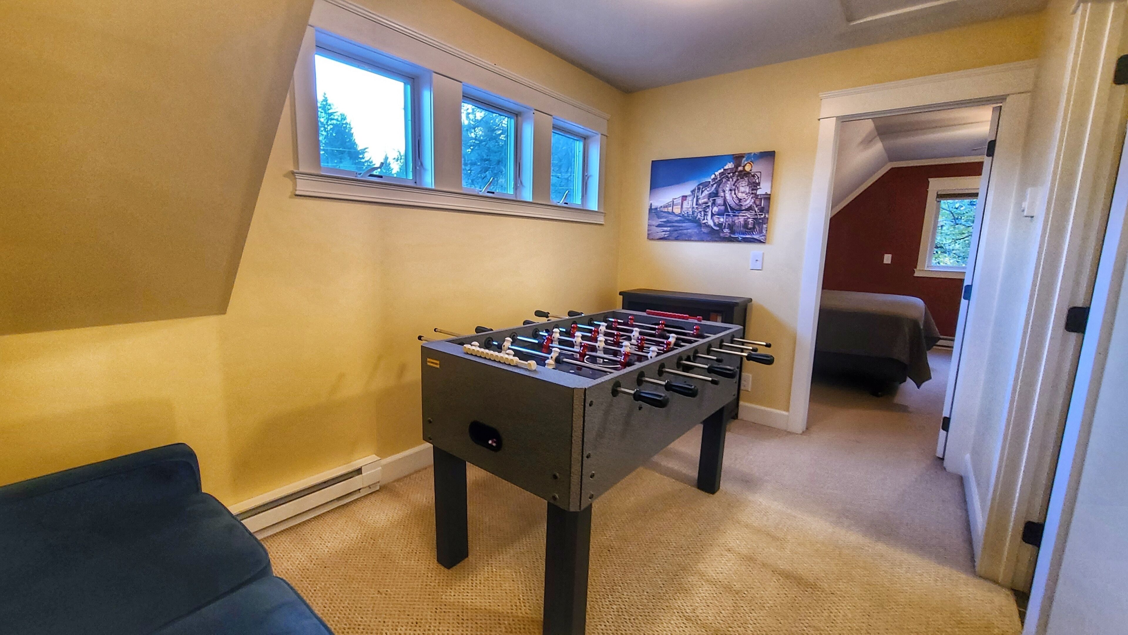 A room with a foosball table, a sofa, and a painting on the wall.