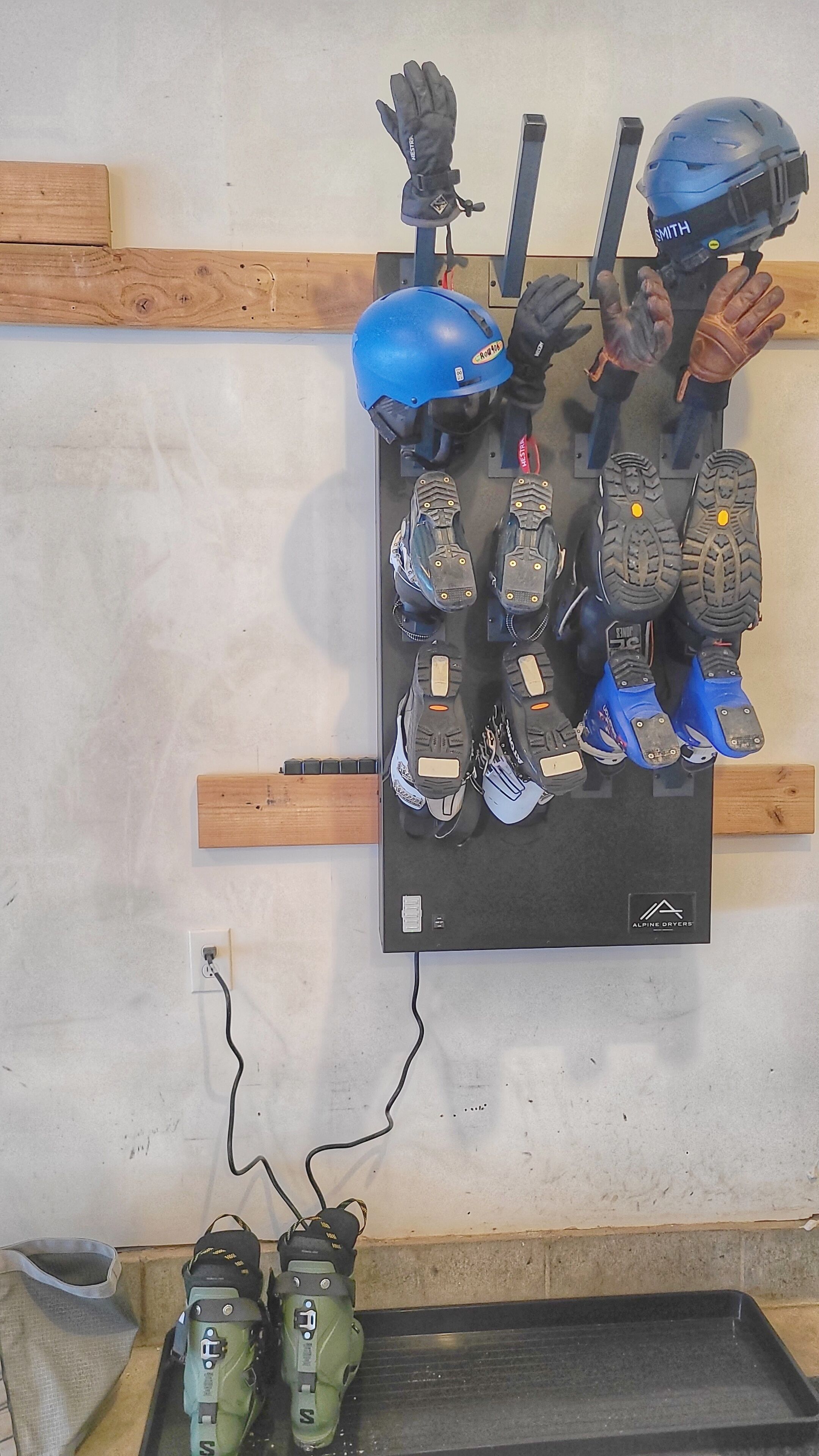 A wall-mounted rack holding various winter sports equipment, including skis, boots, gloves, and helmets.