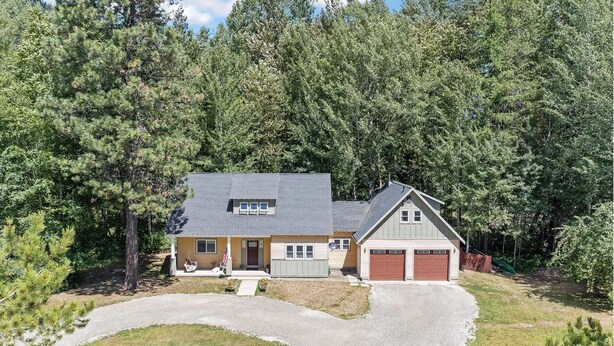 Een huis met twee verdiepingen en een garage, omringd door dicht bos.