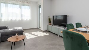 A modern living room with a grey sofa, a wooden coffee table, a TV on a cabinet, and a dining area with green chairs and a table. - Apartment M&M 1 by Interhome (Kaštela)
