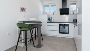 A modern kitchen with white cabinets, a black stove, and a green bar stool. - Apartment M&M 1 by Interhome (Kaštela)