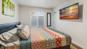 Een slaapkamer met een bed, een raam met zonwering, een schilderij van appels en een schilderij van een zonsondergang aan de muur.