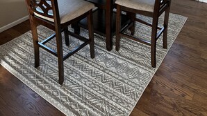 Un coin repas comprenant une table ronde, quatre chaises, un vase de fleurs et un tapis à motifs.