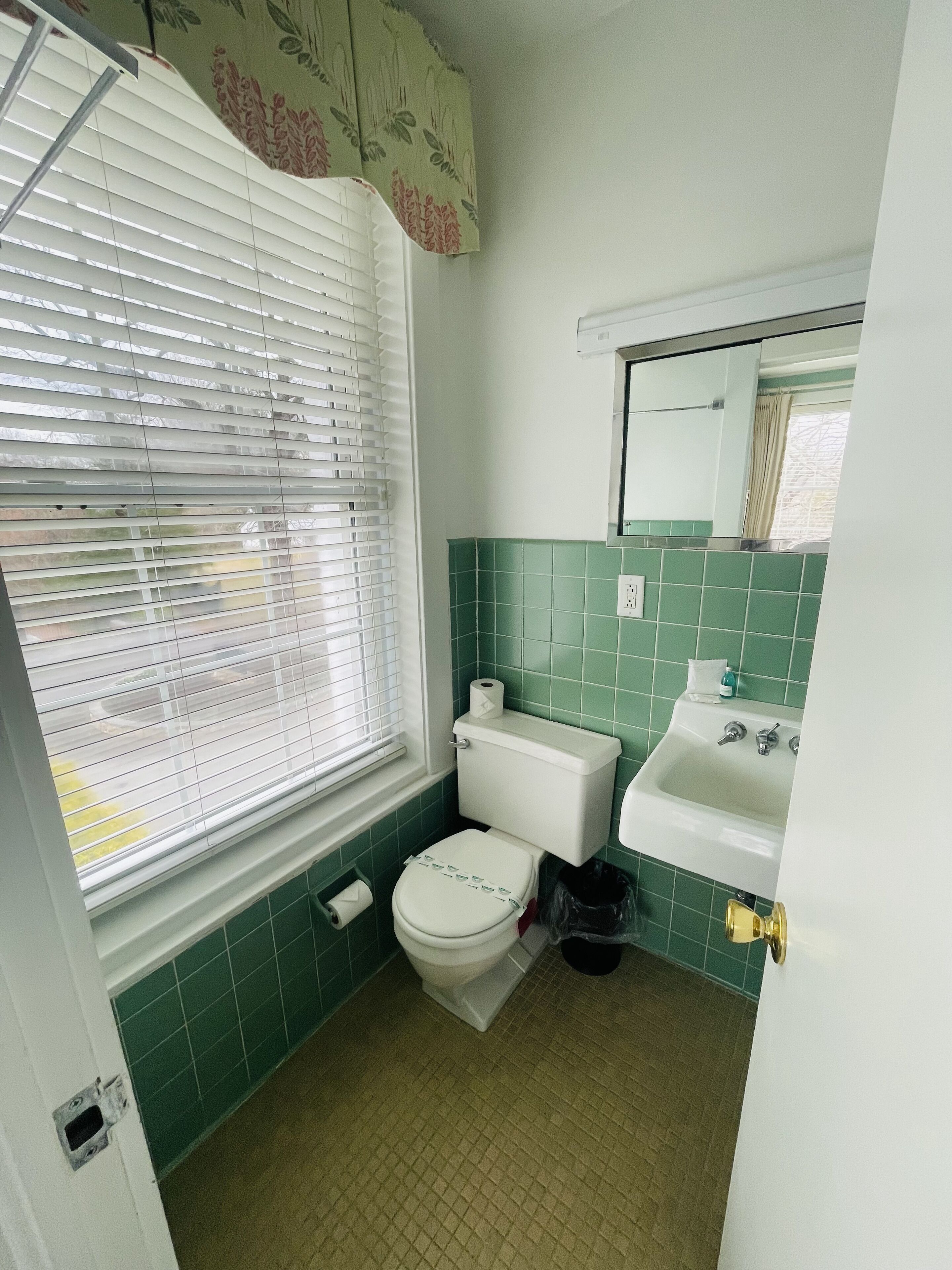 A bathroom with a toilet, sink, and window with blinds.