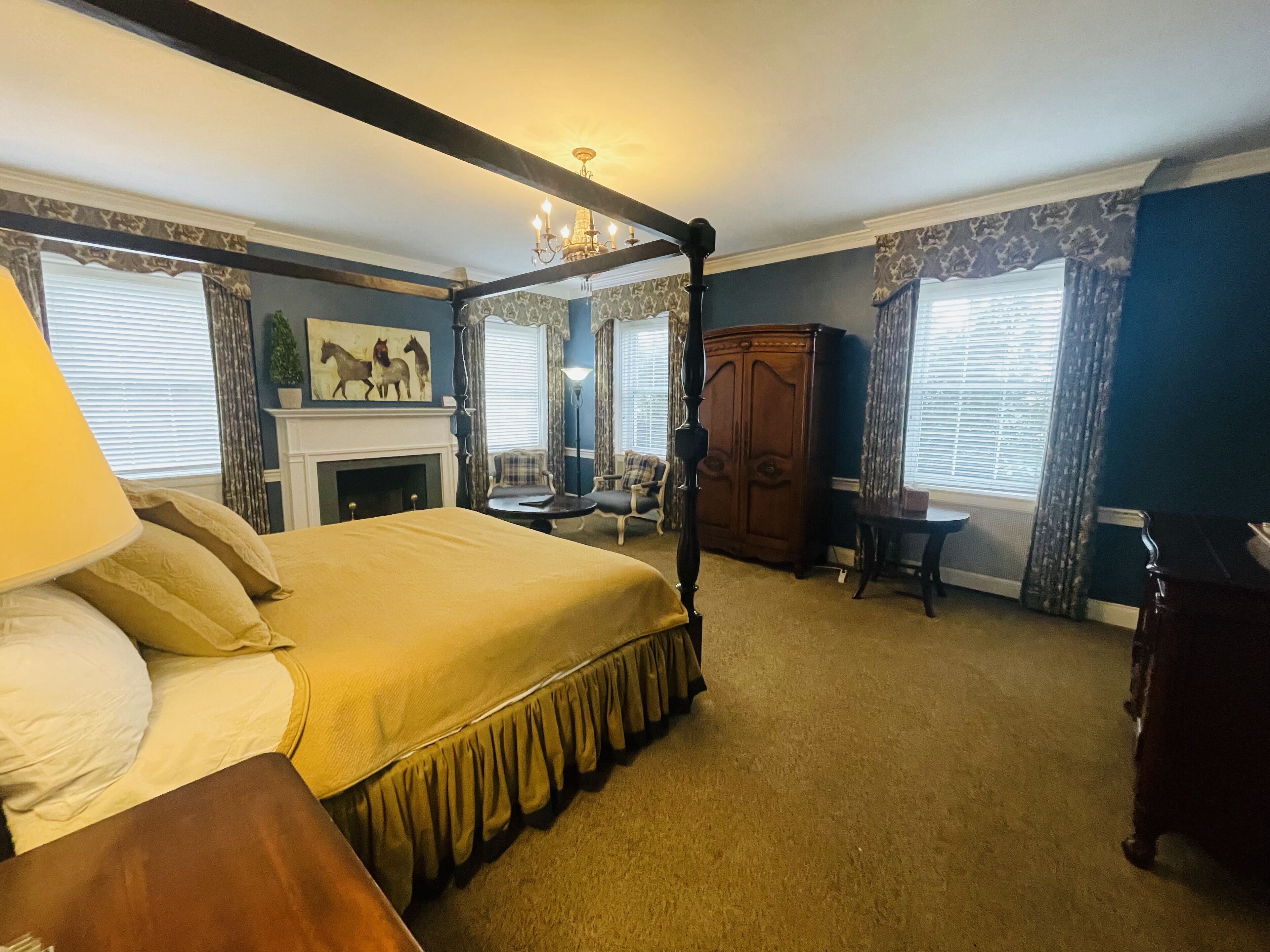 A bedroom with a four-poster bed, a fireplace, a wooden wardrobe, and a small table.