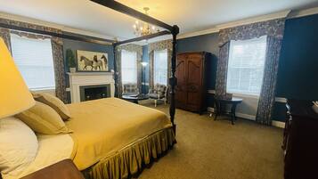 A bedroom with a four-poster bed, a fireplace, a wooden wardrobe, and a small table.