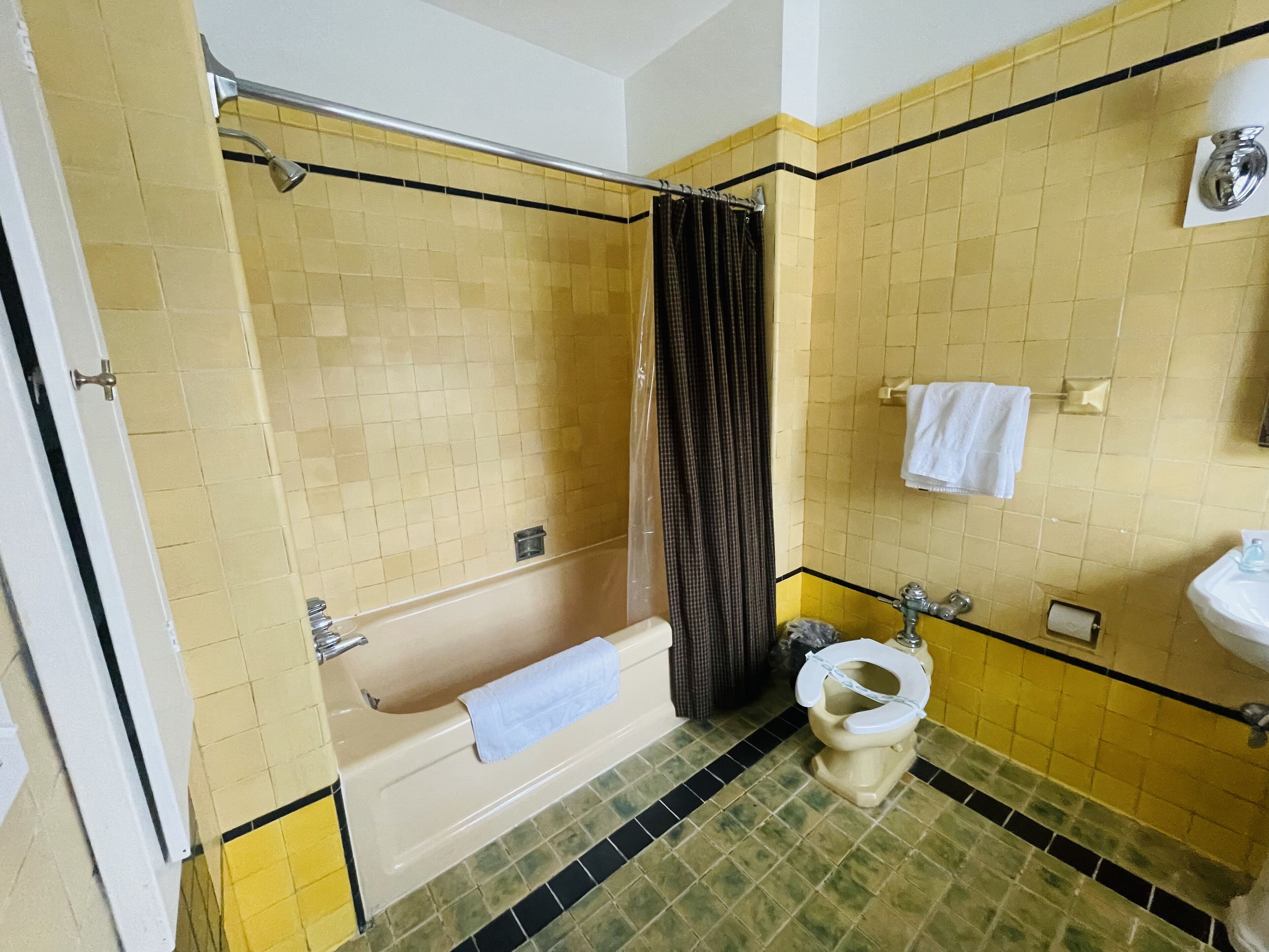 A bathroom with yellow tiled walls, a bathtub, a toilet, and a shower curtain.
