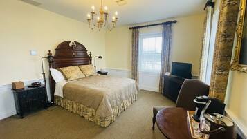 A hotel room with a large bed, a desk with a coffee maker, a TV, and a window with curtains.