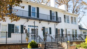 A two-story white building with black shutters, a stone foundation, and a black wrought iron railing. - Excelsior at the Manor House (Clemmons)