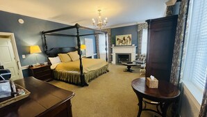 A four-poster bed with a canopy, a fireplace, a dining table, and a chandelier. - Excelsior at the Manor House (Clemmons)