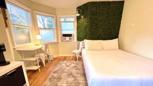 A bedroom with a bed, a desk, and a chair. There are windows with blinds, a radiator, and a green wall. - XL Sacramento Studio Midtown Downtown NEWLY Renovated - Work Play Stay (Sacramento)