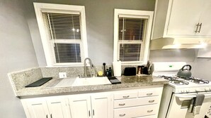 A kitchen with white cabinets, a sink, a stove, and two windows with blinds. - XL Sacramento Studio Midtown Downtown NEWLY Renovated - Work Play Stay (Sacramento)