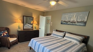 Ein Schlafzimmer mit Bett, Schminktisch, Stuhl, Spiegel, Deckenventilator und einem Bild an der Wand.