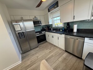 A modern kitchen with stainless steel appliances, white cabinets, a wooden floor, and a window with blinds.