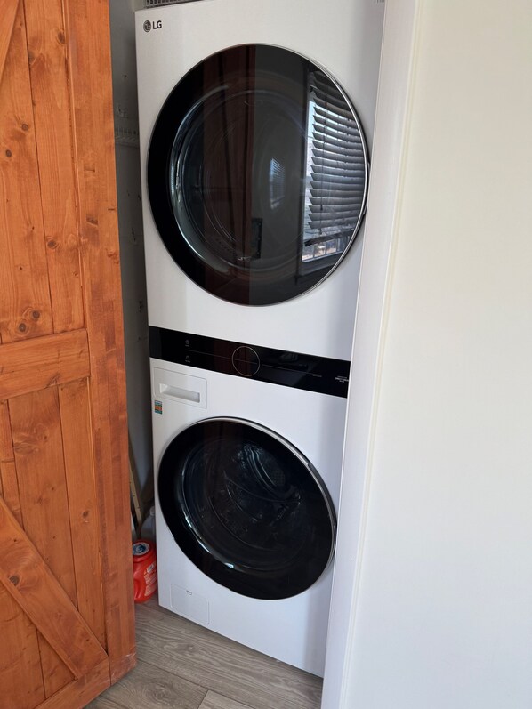 A front-loading LG washer and dryer unit in a corner with a wooden door and a red can on the floor.