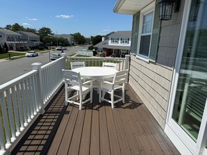 Eine Holzterrasse mit einem weißen Tisch und Stühlen, einem weißen Geländer und Blick auf eine Wohnstraße.