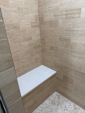 Eine Dusche mit beigen Fliesen und einer weißen Sitzbank.