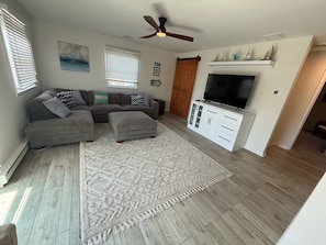 A living room with a sectional sofa, ottoman, TV stand, and a ceiling fan.