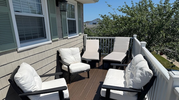 Eine Holzterrasse mit Gartenmöbeln, darunter Stühle und ein Tisch, und einem weißen Geländer.