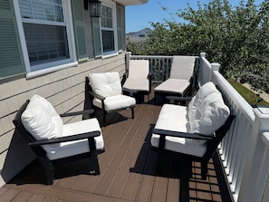 A wooden deck with outdoor furniture, including chairs and a table, and a white railing.