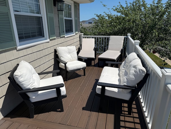 A wooden deck with outdoor furniture, including chairs and a table, and a white railing.