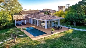 Una casa moderna con piscina, patio y una torre al fondo.