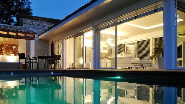 Una casa moderna con piscina, amplios ventanales que dan a una sala de estar y un muro de piedra.