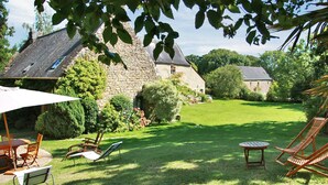 A stone house with a lawn, outdoor furniture, and a large umbrella. - Maison De Charme Dans Le (Brech)