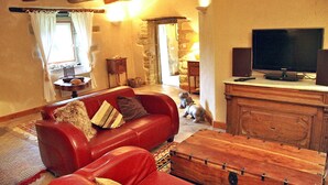 A cozy living room with a red sofa, a wooden coffee table, a television, and stone walls. - Maison De Charme Dans Le (Brech)