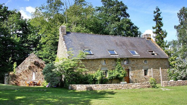A stone house with a sloped roof, multiple windows, and a stone chimney. - Maison De Charme Dans Le (Brech)