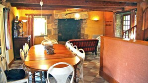 A dining area with a wooden table and chairs, a stone fireplace, and a staircase leading to an upper level. - Maison De Charme Dans Le (Brech)